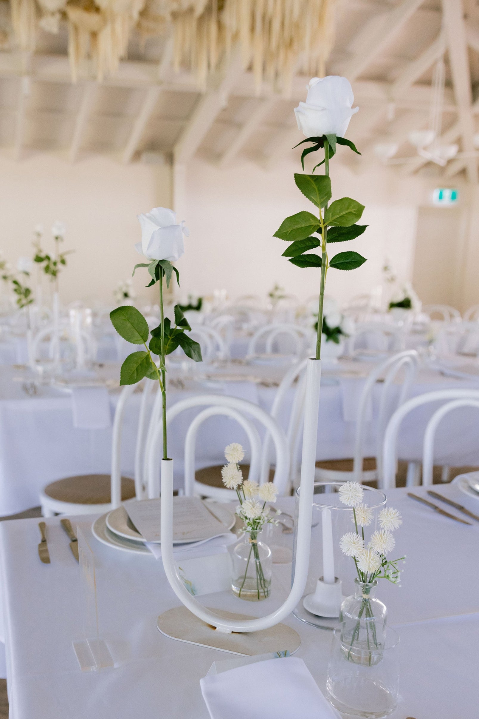 Elegant wedding reception setup with white tablecloths, silverware, and floral centerpieces.